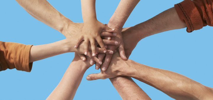 Acht Hände liegen aufeinander und symbolisieren den gemeinschaftlichen Gedanken von Genossenschaften.