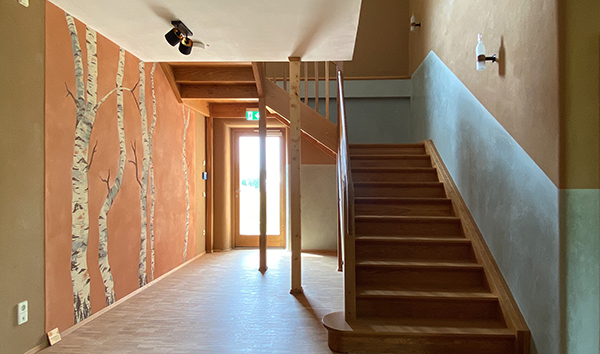 Flur mit großer Holztreppe und Wandgemälde im Strohtel. Das Wandgemälde ist Teil des Nachhaltigen Kunstkozepts des Gebäudes