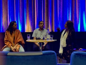 Drei Personen sitzen auf dem Podium und sprechen.