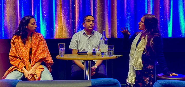 Drei Personen sitzen auf dem Podium und sprechen.