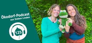 Aniko und Simone stehen vor einer grünen Hecke und halten einen Stofftierfrosch in ihrer Mitte.