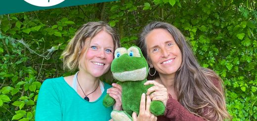 Aniko und Simone stehen vor einer grünen Hecke und halten einen Stofftierfrosch in ihrer Mitte.