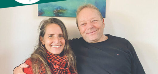 Pablo und Simone stehen Arm in Arm vor einer Wand und schauen freundlich in die Kamera