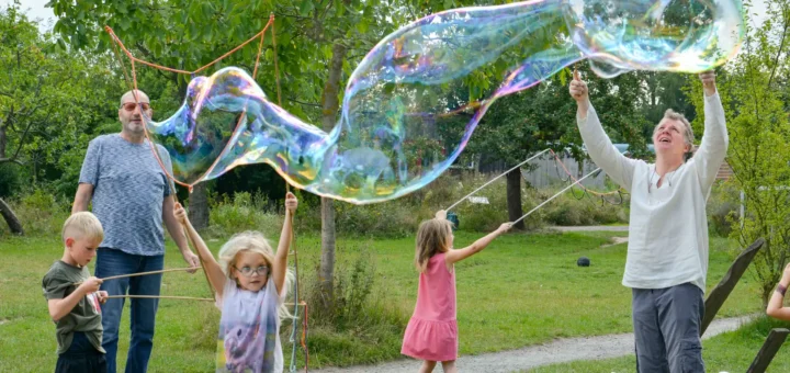 Kinder und Erwachsene machen riesiege Seifenblasen zusammen